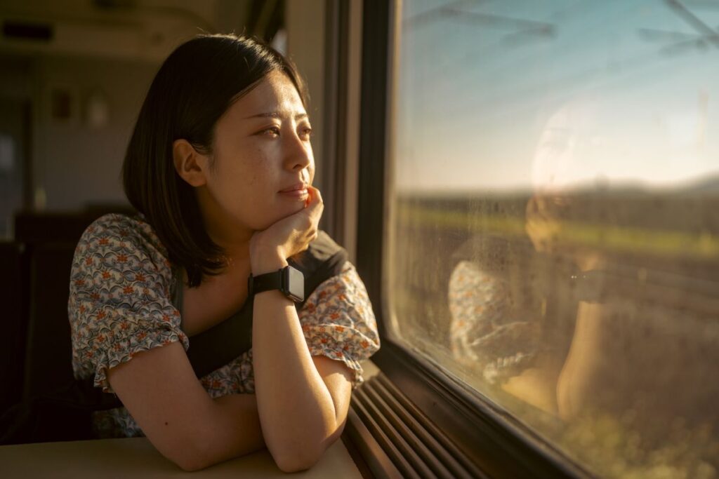 Portrait of young female tourist traveling by train. She is sitting at the seat next to the window and looking outside at the view through the window.