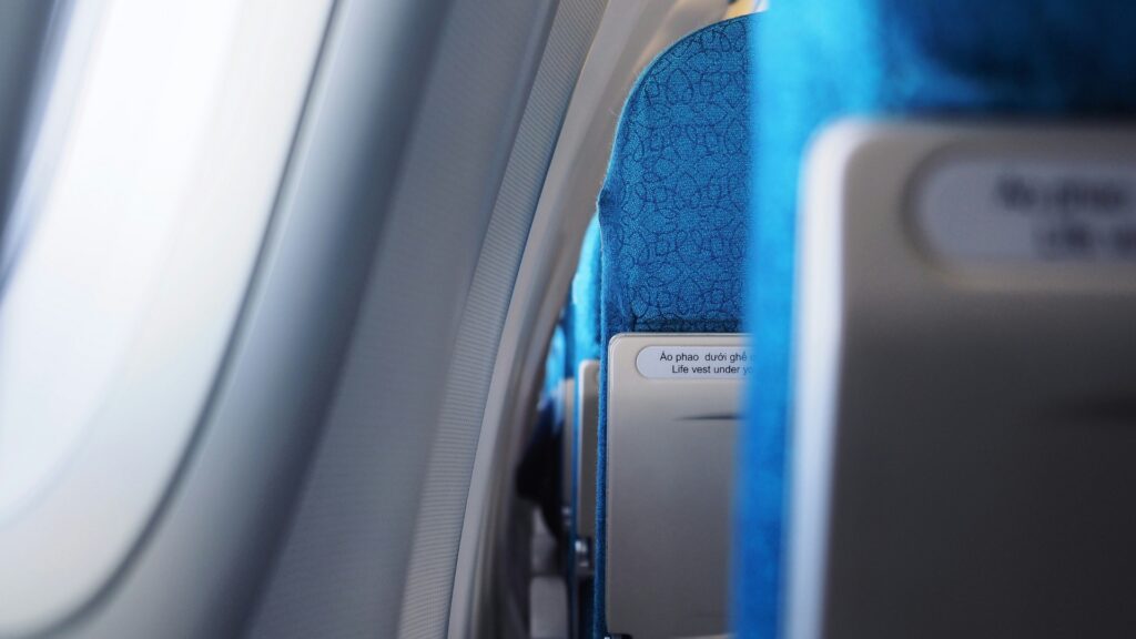 View inside an airplane cabin with bright blue patterned seats beside a sunlit window.