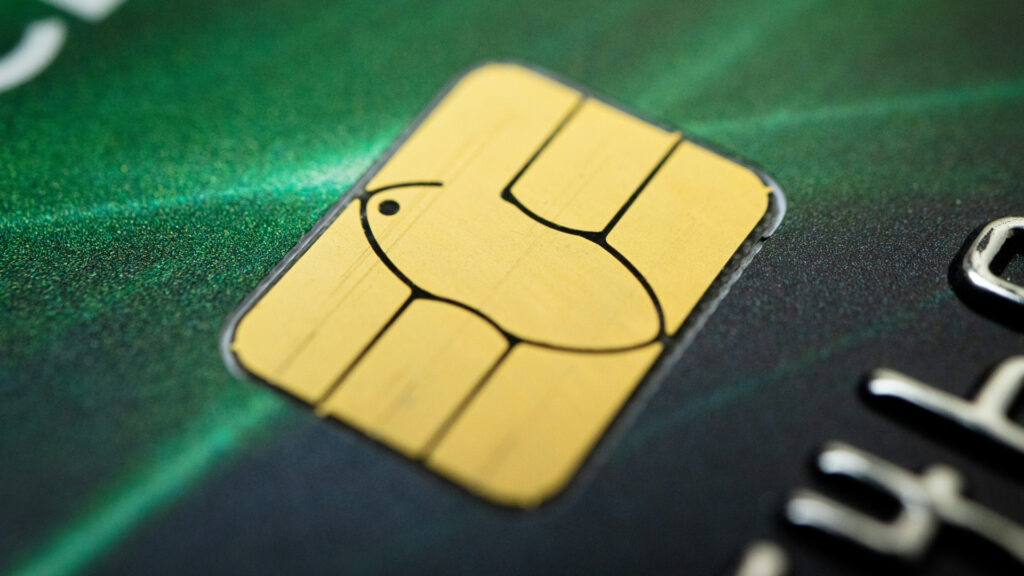 Extreme close up of the gold electronic chip embedded in a green payment card. The metallic contact sections and curved circuit pattern fill most of the frame.