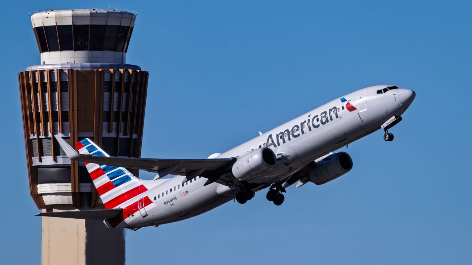 American Airlines Ends Free Business Upgrades While Adding Premium Economy American Airlines passenger jet takes off beside an airport control tower, climbing against a clear blue sky in bright daylight.