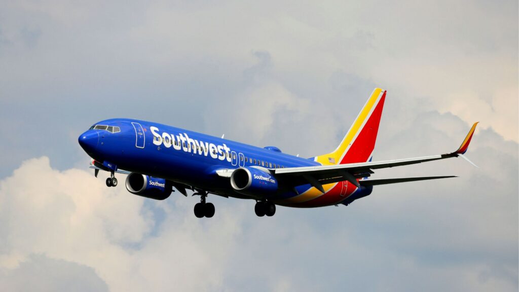 Southwest Airlines Boeing 737 flies with landing gear down against a cloudy sky, its blue fuselage and vivid red-and-yellow tail prominent.