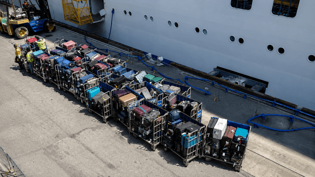 Rows of passenger luggage lined up on carts beside a large cruise ship at port.