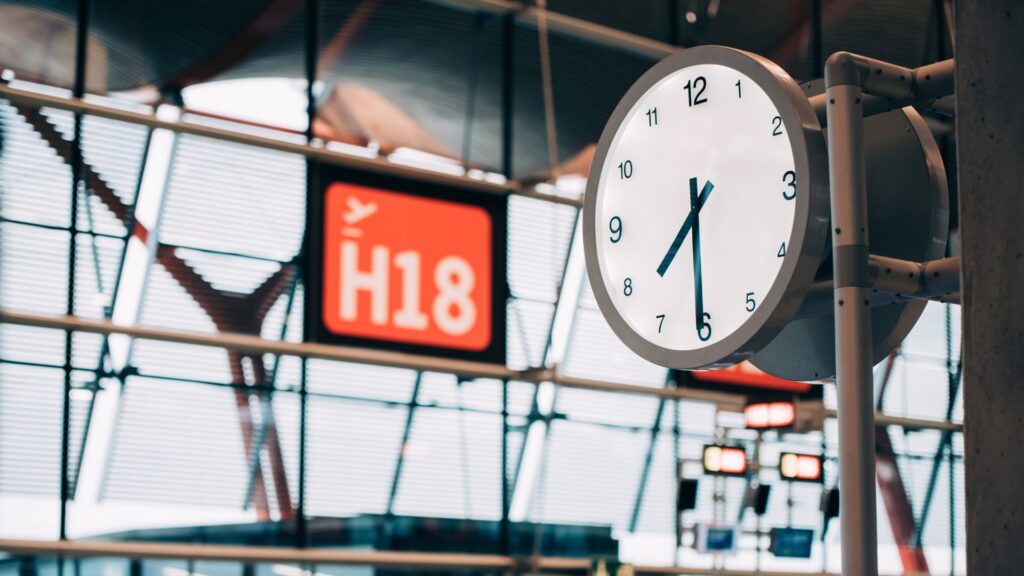 Round clock beside an orange gate sign in an airport terminal.