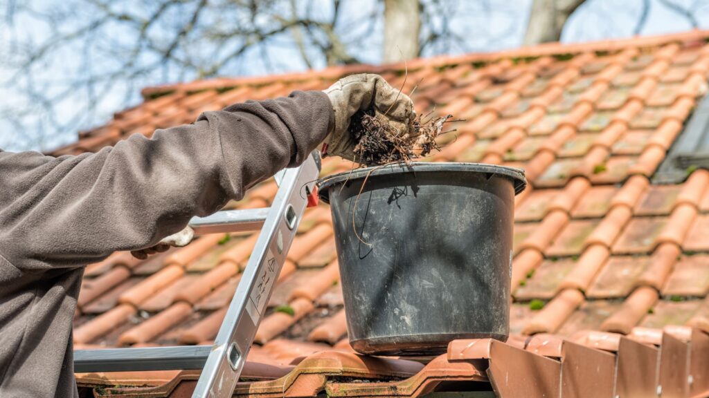 A man on a ladder cleaning house gutters.