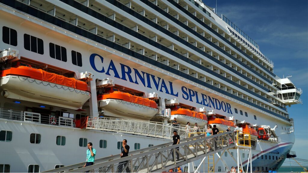 Carnival Splendor cruise ship docked at port, with orange lifeboats, and passengers on a gangway.